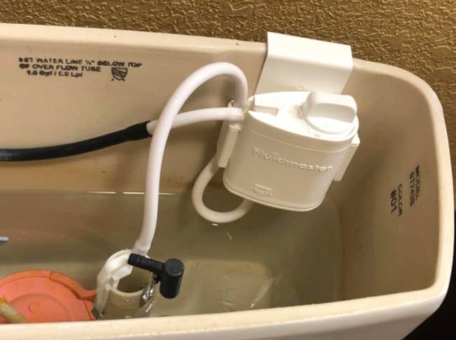 A reviewer's installed system, which clips on to the tank and attaches to two of the toilet's internal tubes