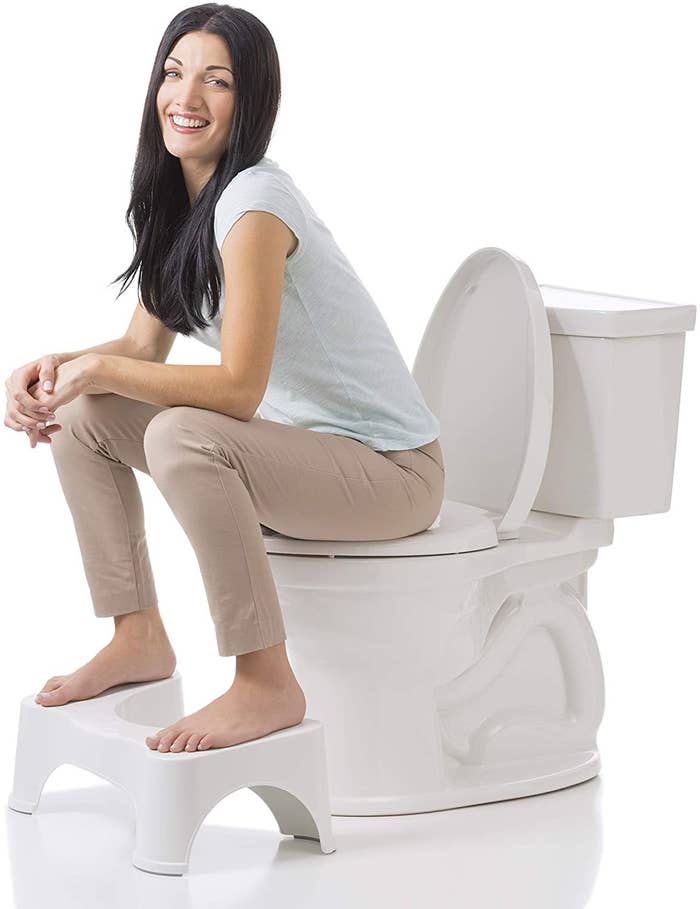 A person sitting on a toilet with a small stool under their feet