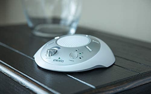 A hand-sized white noise machine on a bedside table 