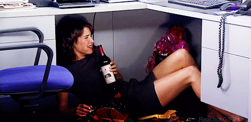 A GIF of Robin from How I Met Your Mother crying under her desk while drinking wine
