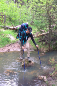 A different reviewer using the hiking poles to balance on a rock while crossing a stream 