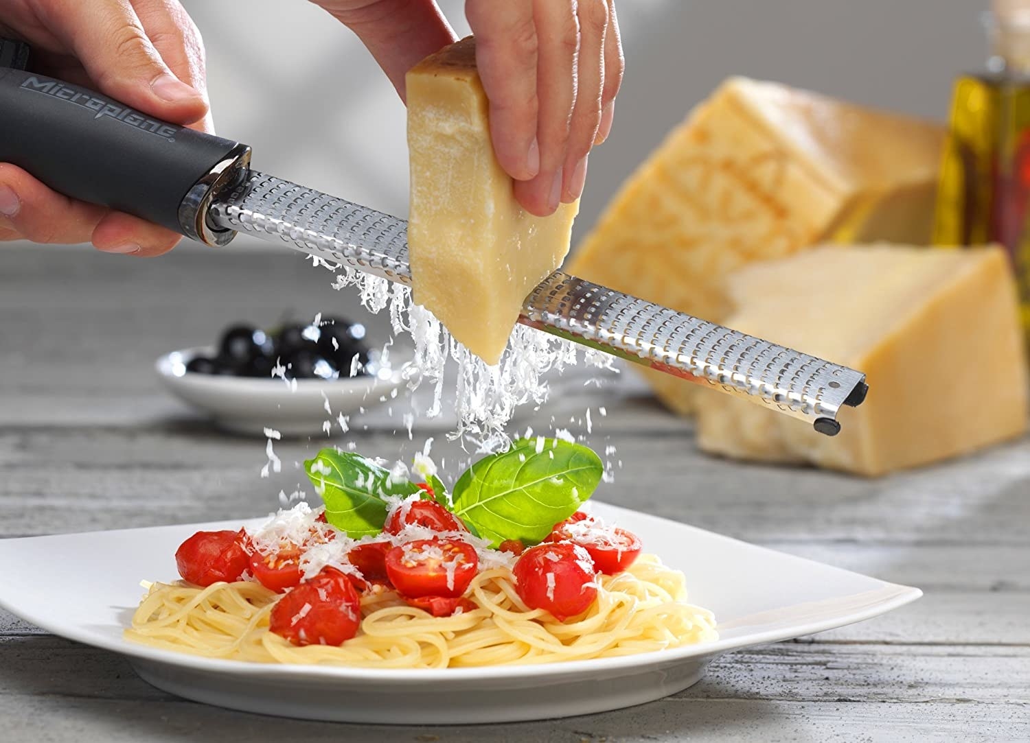 The microplane grating a block of cheese over a plate of pasta