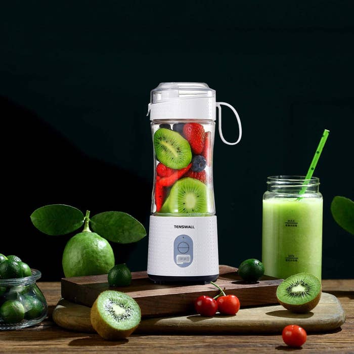 A white blender with clear plastic up filled with strawberries blueberries, and kiwis