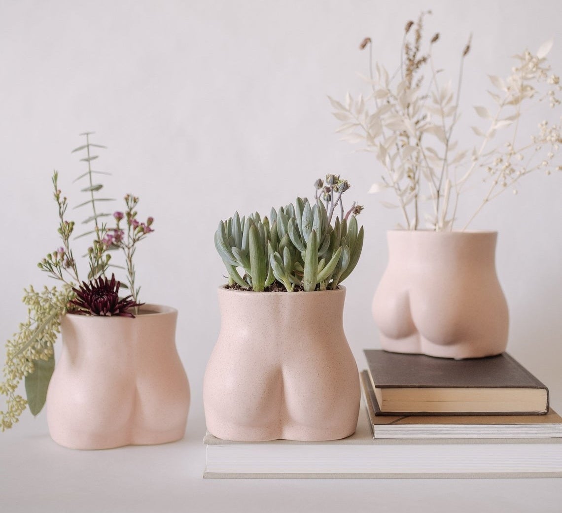 Multiple of the Body Vases (shaped like butts) filled with floral arrangements. 