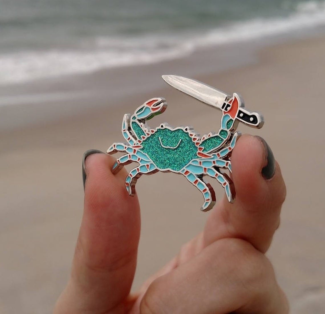 A person holding the enamel Stabby Crab pin.