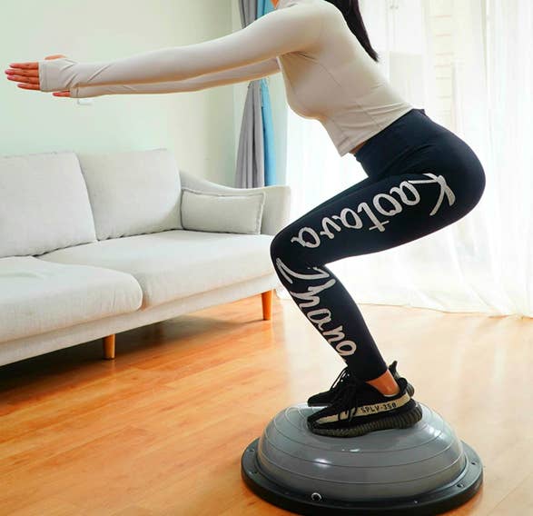Model uses gray balance ball trainer to do a squat in her living room