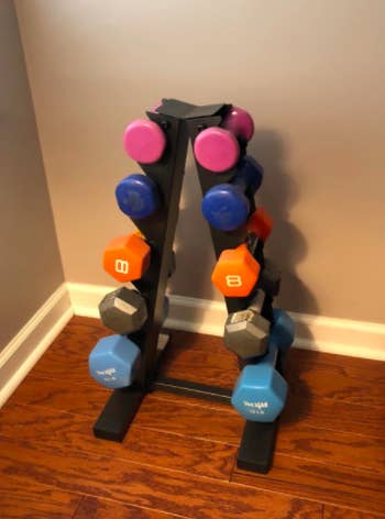 Reviewer uses black dumbbell weight rack to hold their eight and five-pound weights against a wall