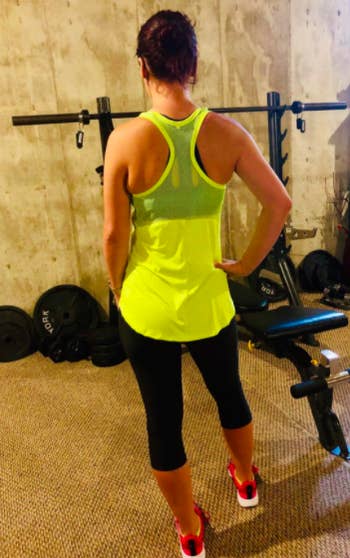 Reviewer wears same style tank top in a yellow color with black workout capris