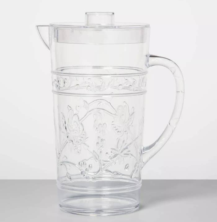A glass pitcher with a lid and floral designs 