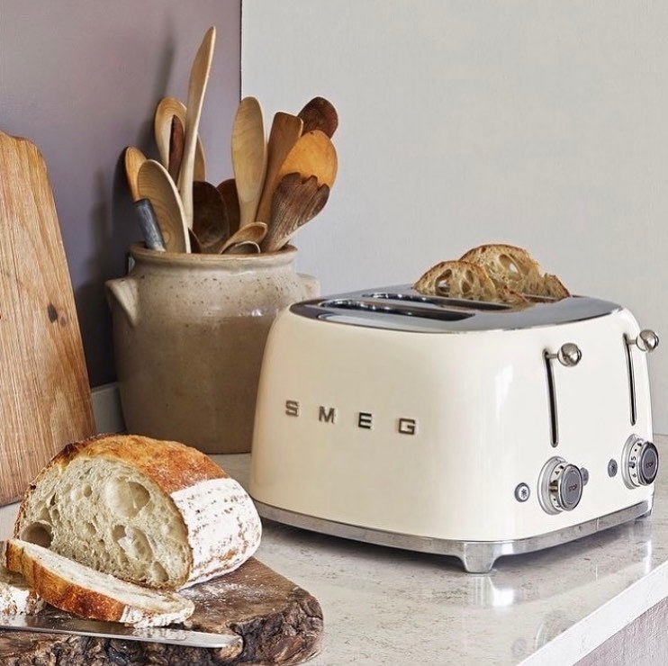 a white smeg toaster with freshly cut bread in it and next to it