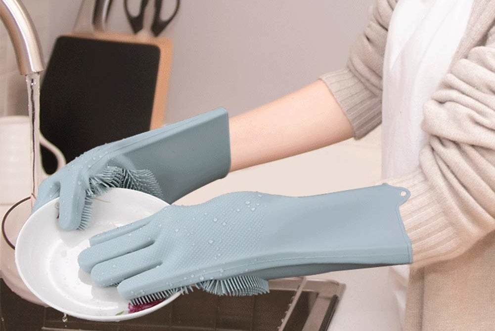 A person washing a plate with grey silicone cleaning gloves on.