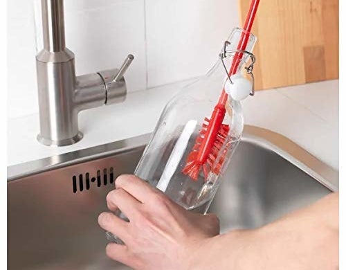 A glass bottle being cleaned with a red brush.