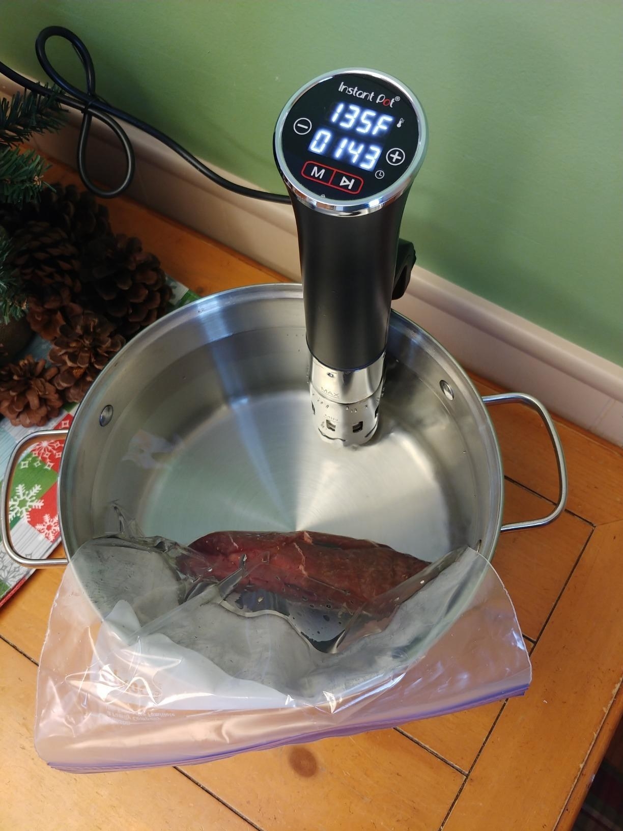 The sous vide immersion circulator in a pot with a bag of meat