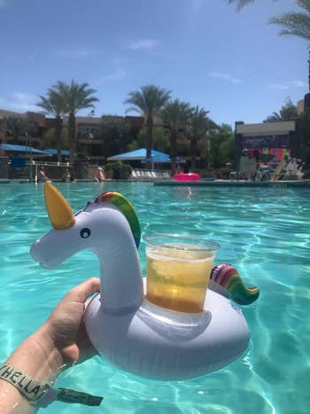 A reviewer holding up the unicorn float with a drink being held in the middle