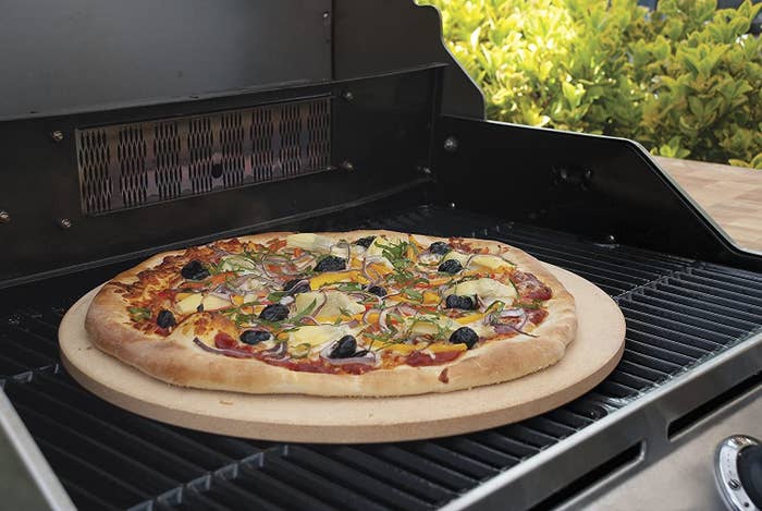 A homemade pizza on the Pizzacraft stone on an outdoor grill.