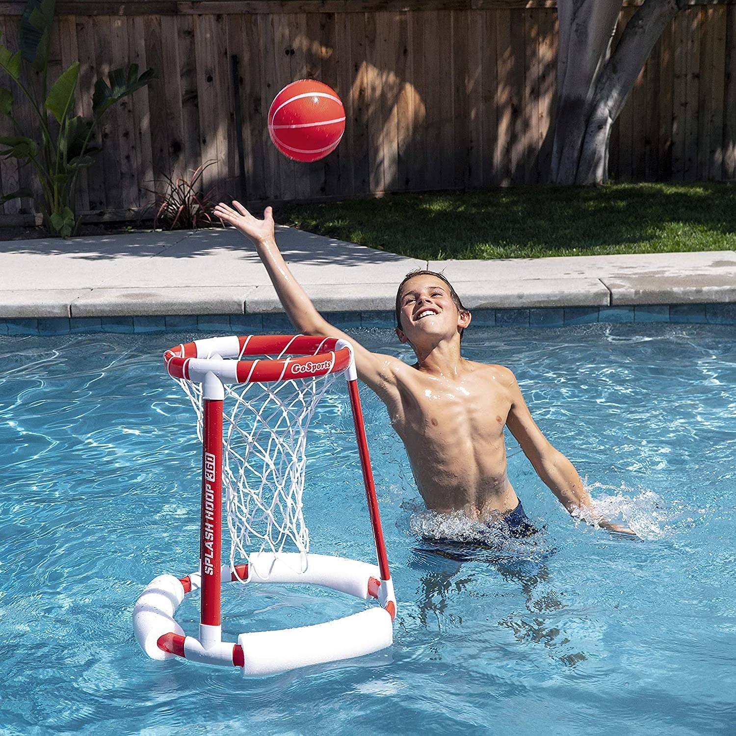 A kid throwing a ball into the hoop floating in the pool