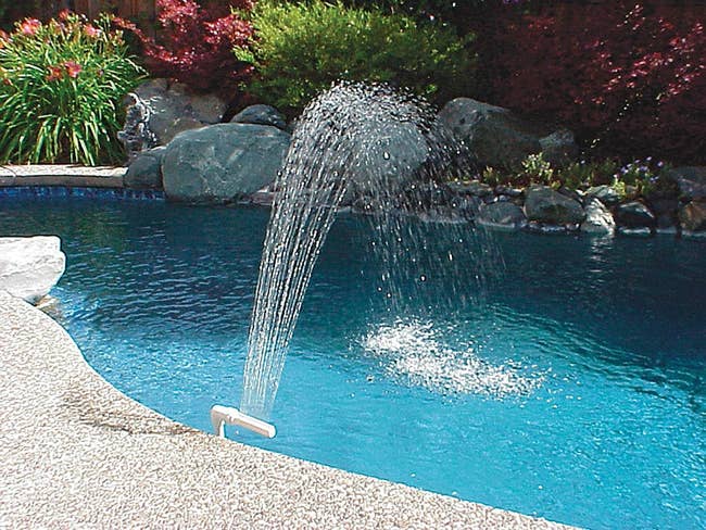 The sprinkler on the edge of the pool creating a stream that lands back inside the pool