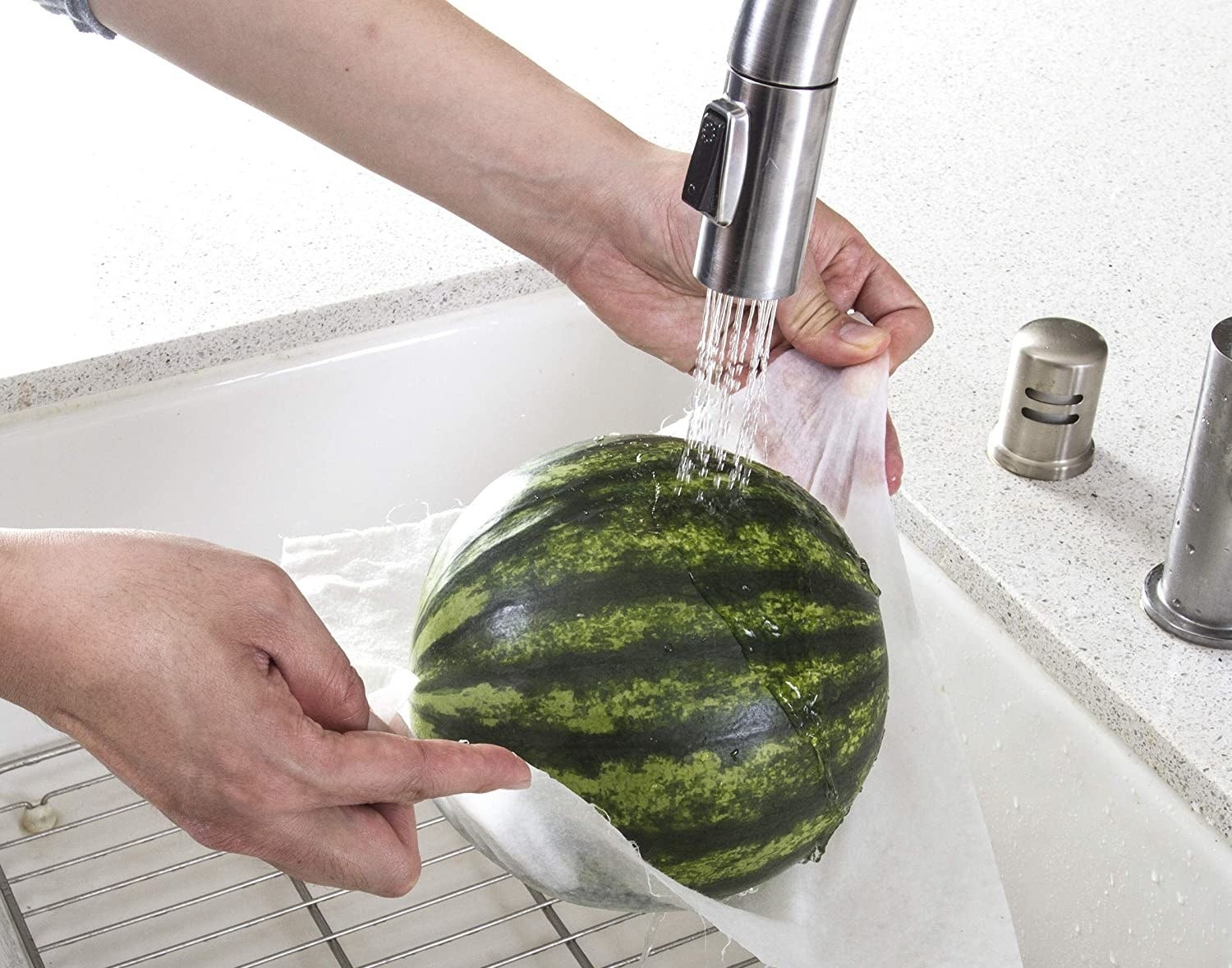 model washes a watermelon while holding it up with wet paper towel