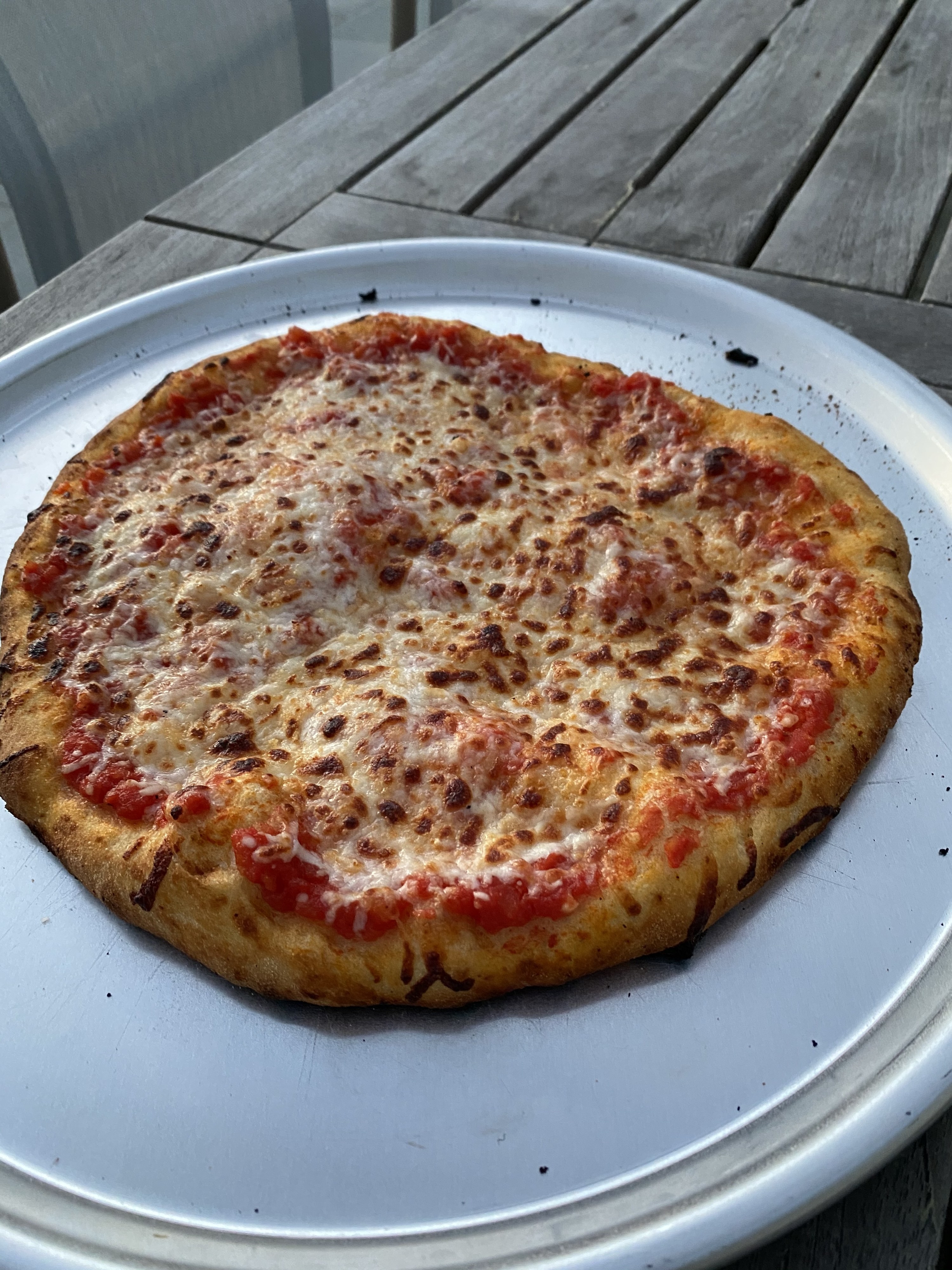 A freshly cooked pizza, just out from the pizza oven with charred crust and golden brown cheese.