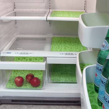 open refrigerator door with green liners on the shelves and four of the glass sections