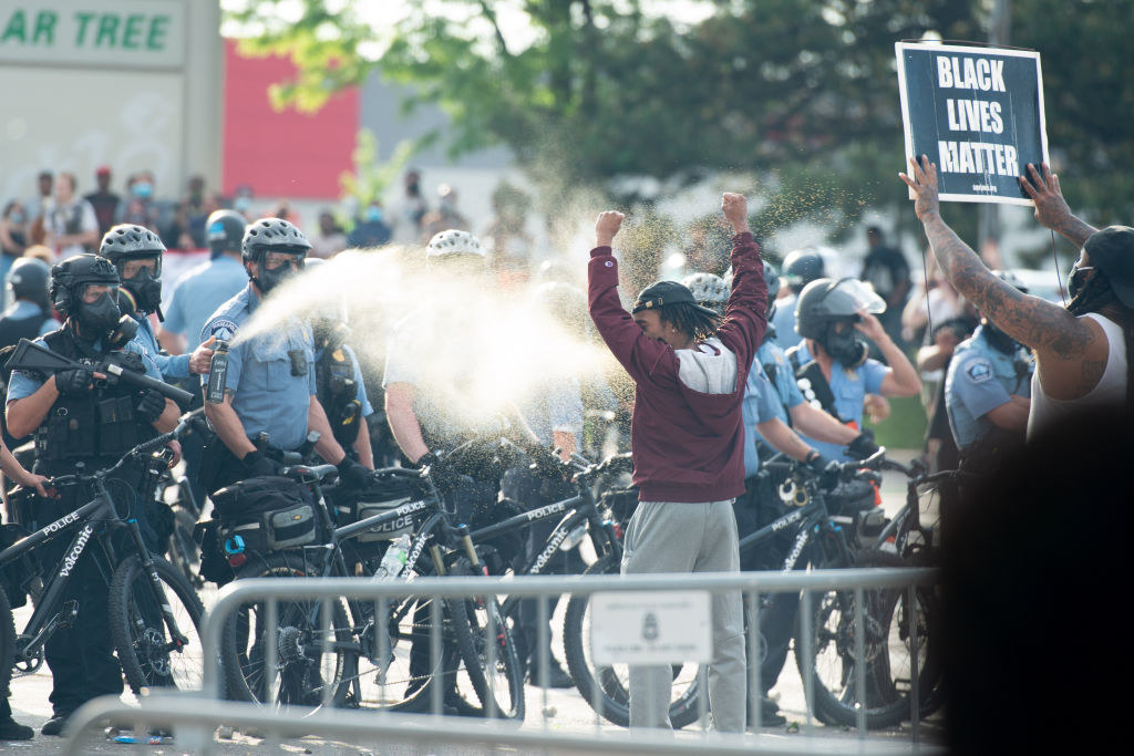 Police officer pepper sprays man who&#x27;s holding his arms up directly in the face