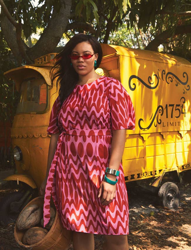 A model wearing the red and pink patterned dress, it falls right at the knee and has a tie at the side