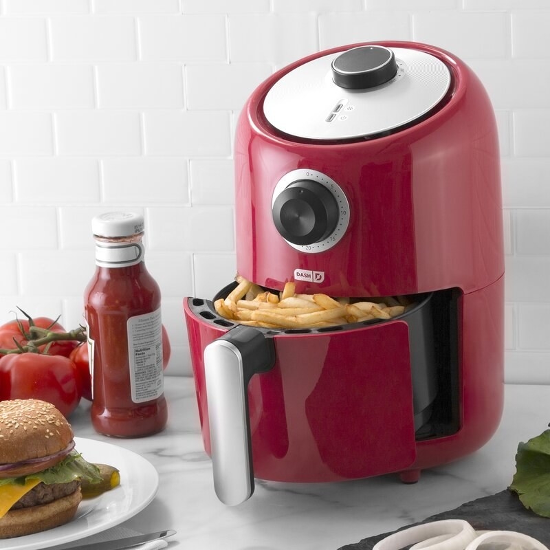 The air fryer in red, featuring a round analog timer and a handle on the frying basket 