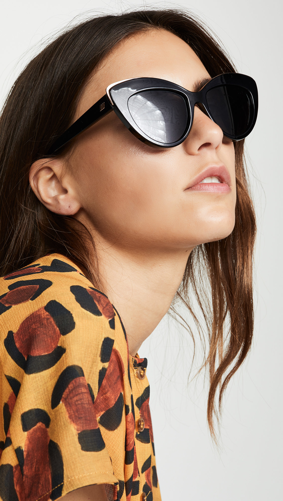 a model wearing the sunglasses: they have a thick cat-eye shape, are black, and have a subtle gold accent along the top of the rims
