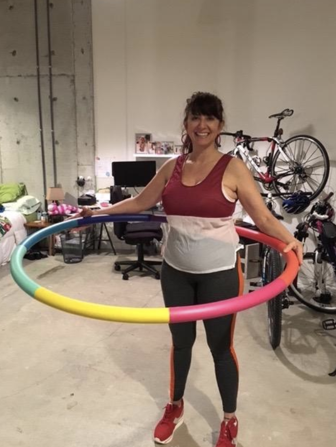 Reviewer works out with a rainbow weighted sports hoop in their garage
