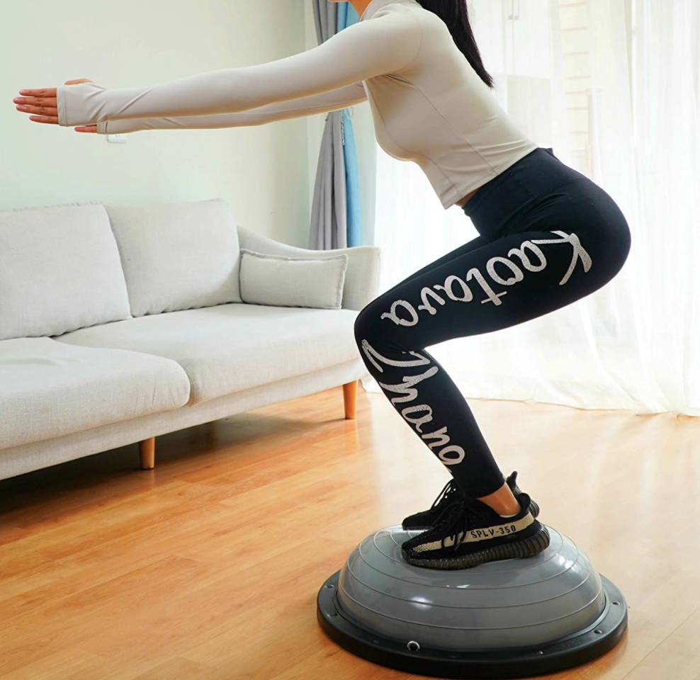 Model squats on a gray balance ball trailer in their living room