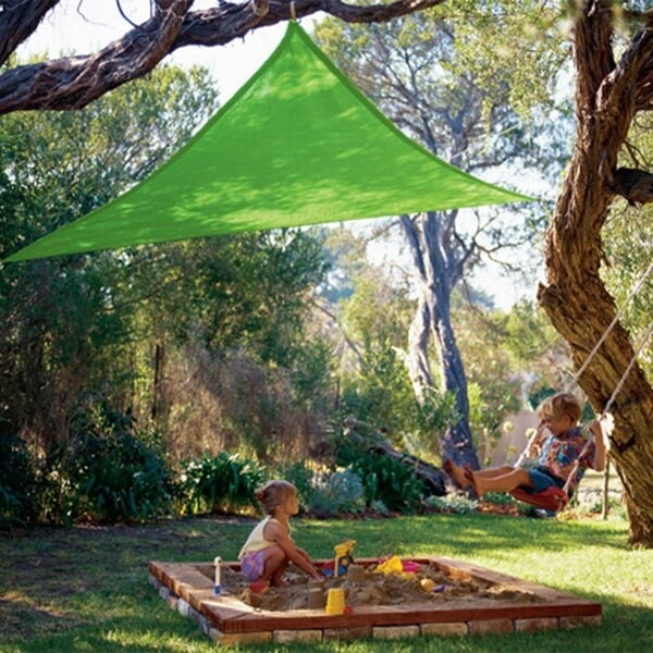 kid playing in sandbox with a green triangle sail overhead attached to tree branches
