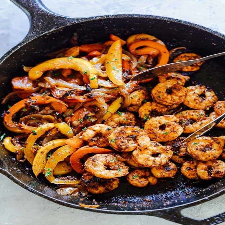 Shrimp, peppers, and onions cooking in a skillet with fajitas spices.