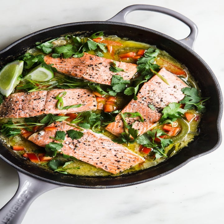 Salmon fillets in a green curry sauce in a skillet with fresh herbs, peppers, and lime.