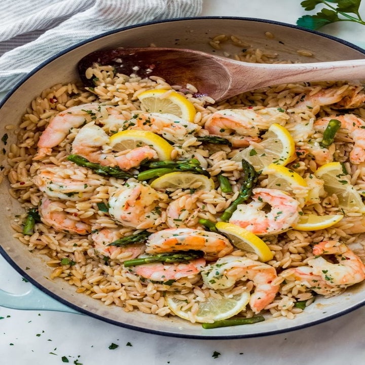 A skillet with shrimp, orzo, and asparagus.