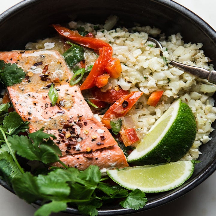 A bowl with rice, salmon, peppers, lime, and herbs drizzled with green curry sauce.