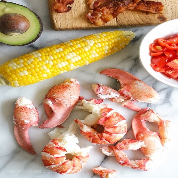 Ingredients for lobster cobb salad including cooked lobster meat, corn on the cob, avocado, and tomato.