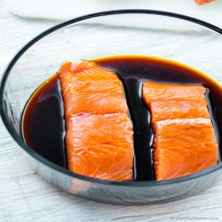 Two salmon filets marinating in a soy sauce mixture.