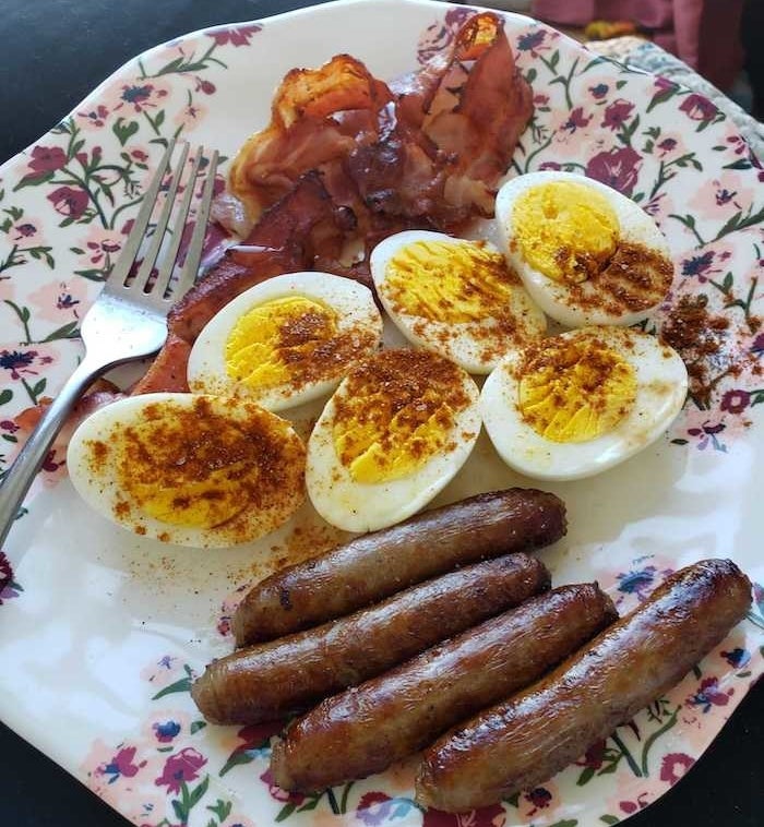 Three split boiled eggs on a plate with sausage links and bacon strips