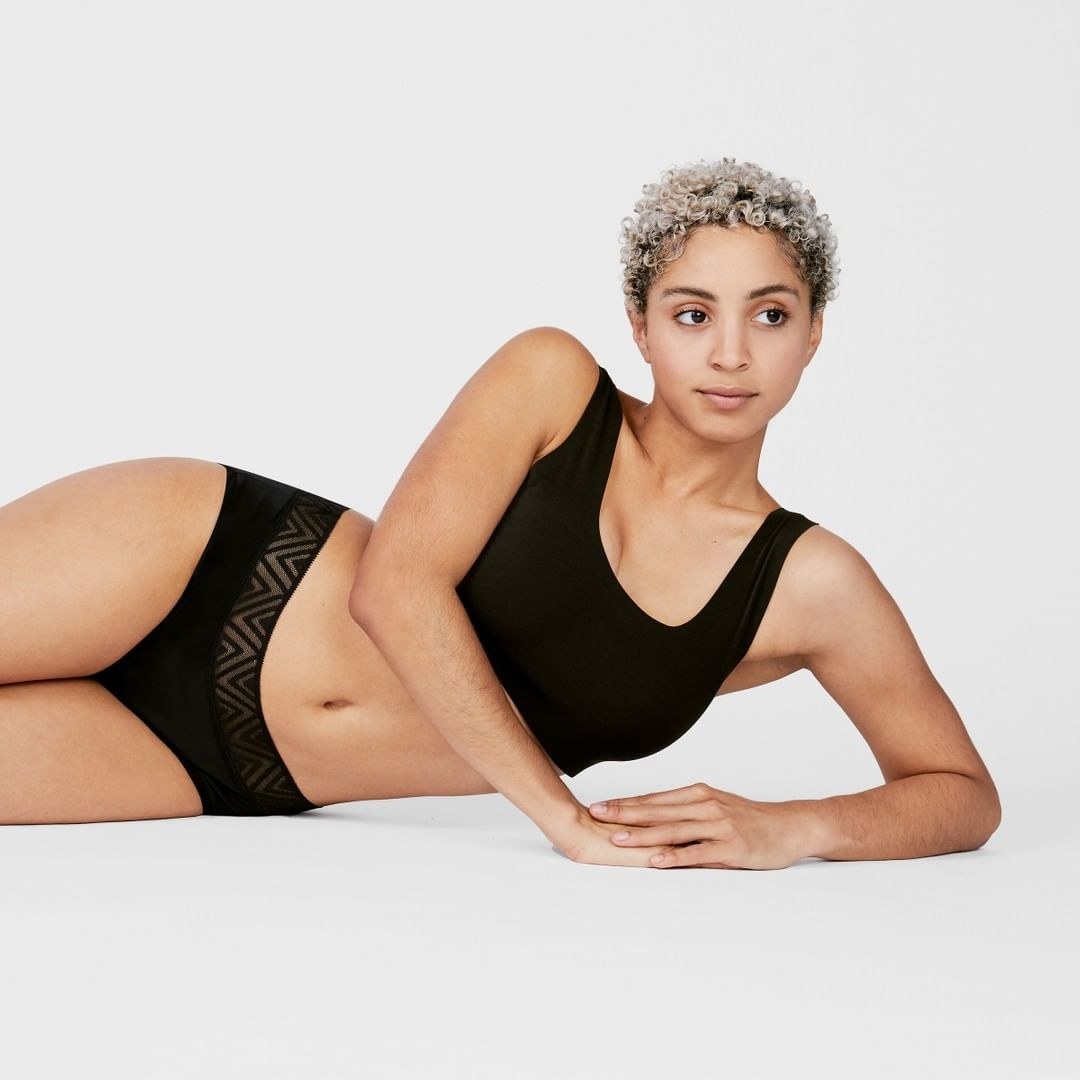 A model wearing black Thinx underwear with a sports bra 