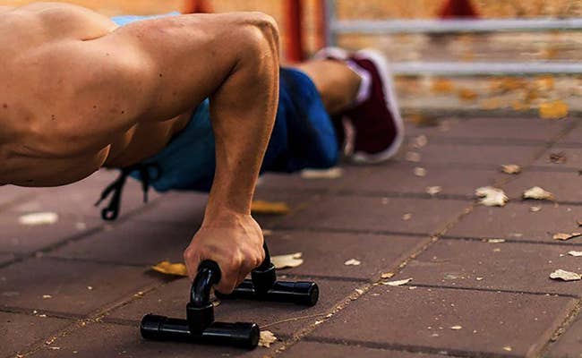 A model uses black push-up bars while exercising on an outdoor patio