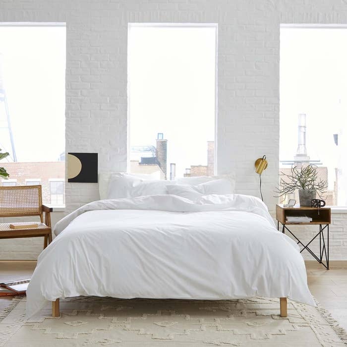 a bedroom with bright windows showcasing a cozy bed with a white comforter and white sheets