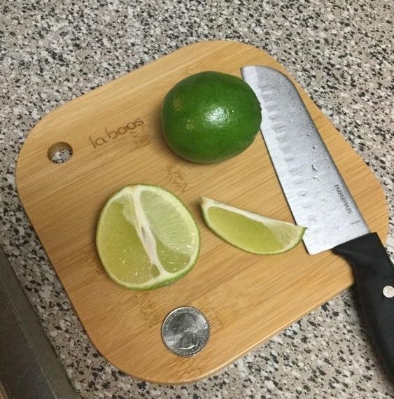 Reviewer&#x27;s picture of the mini bamboo cutting board being used to cut limes