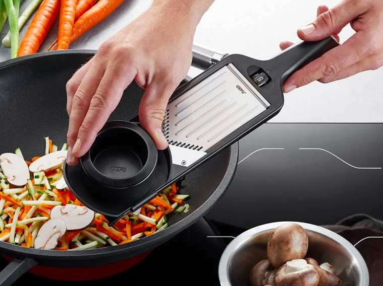 person holding the tool over a frying pan while using it to slice mushrooms into the pan