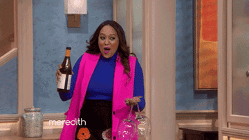 Gif of Tina Mowry walking in with a bottle of wine and two wine glasses