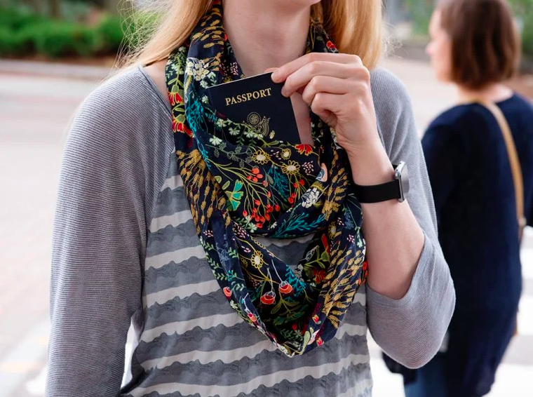 person wearing an loop-style scarf around neck and tucking passport into secret pocket in the scarf