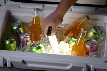 A hand reaching inside the lit-up cooler to grab a drink 