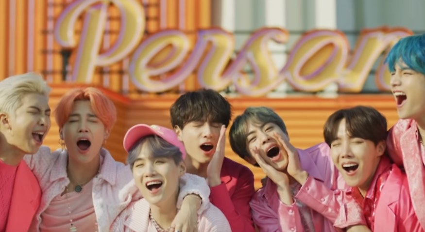 The members of BTS embrace while wearing all pink and yelling happily