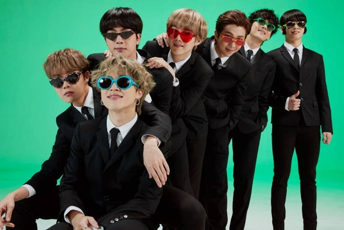 BTS wear suits and novelty sunglasses while lined up in a green studio