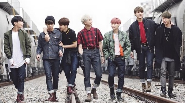 BTS walk in a line along train tracks; they wear casual clothes
