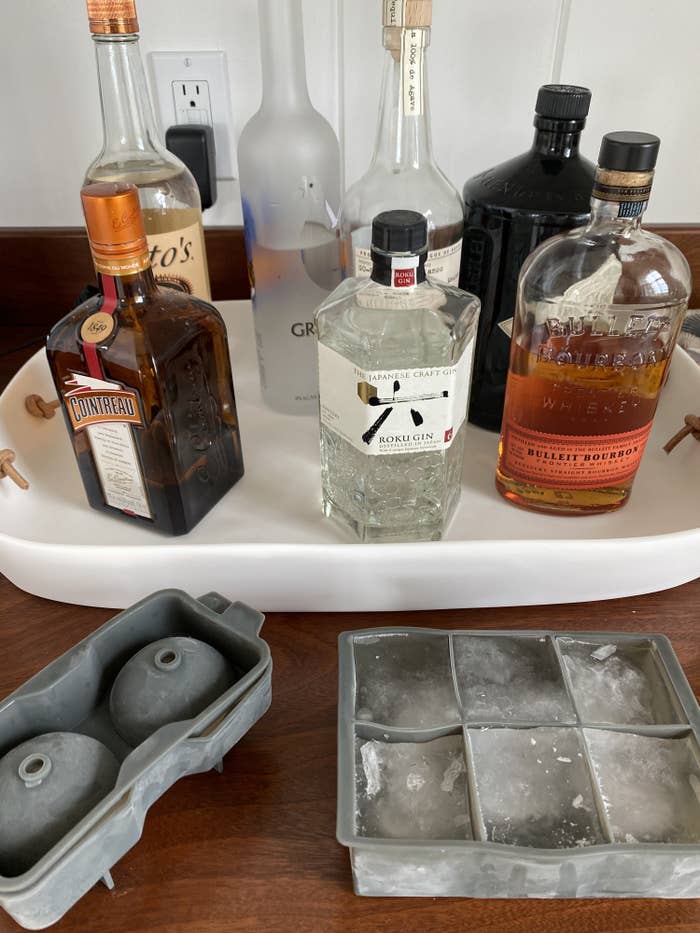 A wet bar with bottles of alcohol and two sets of jumbo ice cube molds-- one spherical and one square. 